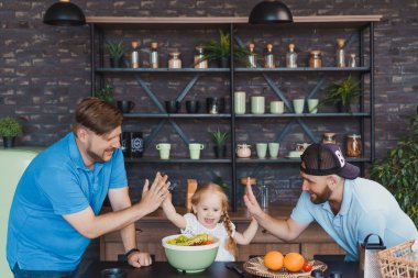 Eşcinsel ebeveynler kızlarıyla yemek pişiriyor ve beşlik çakıyor.