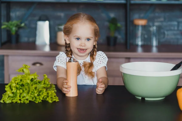 Κοριτσάκι που κρατάει μύλο πιπεριού, κάθεται στο τραπέζι της κουζίνας. — Φωτογραφία Αρχείου