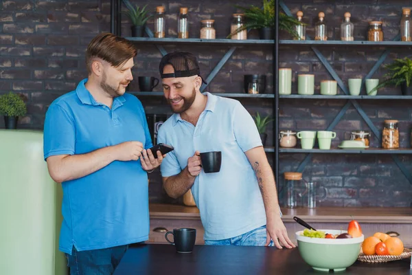 Gay paar in de keuken. Vrienden drinken thee en gebruiken een telefoon — Stockfoto