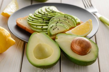 Avokado yarımları ve dilimli tost. İçindekiler beyaz ahşap masada.