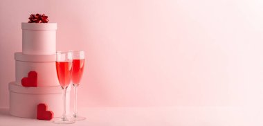Yuvarlak hediye kutuları, kırmızı şarap bardakları ve pembe üzerine iki kalp.