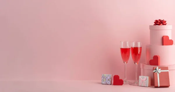 Vasos de vino espumoso rojo, cajas de regalo y corazones rojos sobre fondo rosa — Foto de Stock