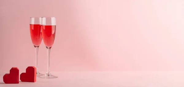 Two glasses of prosecco and red hearts on pink background