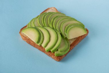 Mavi arka planda avokado dilimli tost.