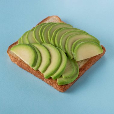 Mavi arka planda dilimlenmiş avokadolu tost.