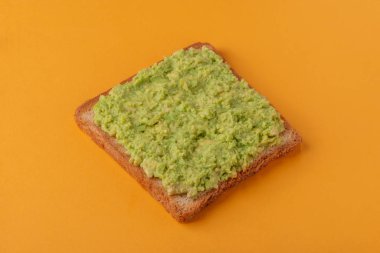 Turuncu arka planda ezilmiş avokado ile çıtır tost.