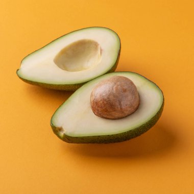 Turuncu arka planda çekirdekli yarım avokado.