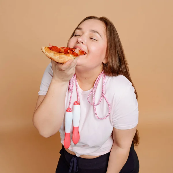 Mujer gorda comiendo rebanada de pizza sobre fondo beige —  Fotos de Stock