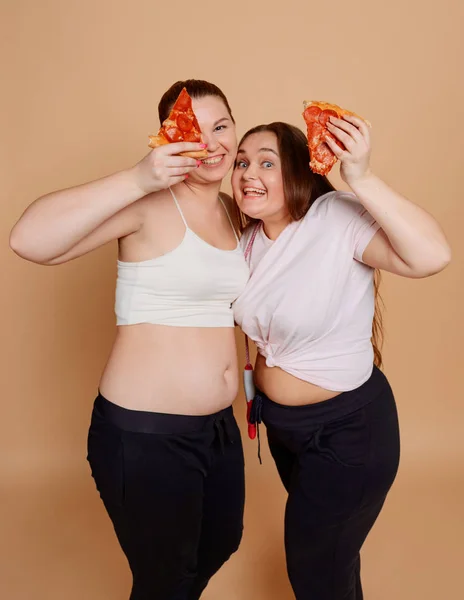 Dziewczyny jedzące pizzę na beżowym tle. Przejadanie i tłuszcz z brzucha — Zdjęcie stockowe