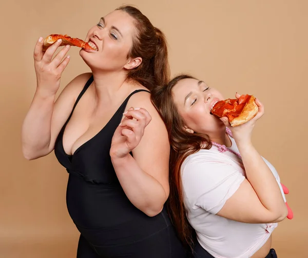 Hungry fat woman eating pizza on beige background