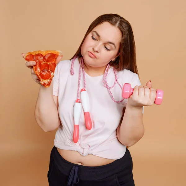 Chica ejercitando y queriendo pizza sobre fondo beige —  Fotos de Stock