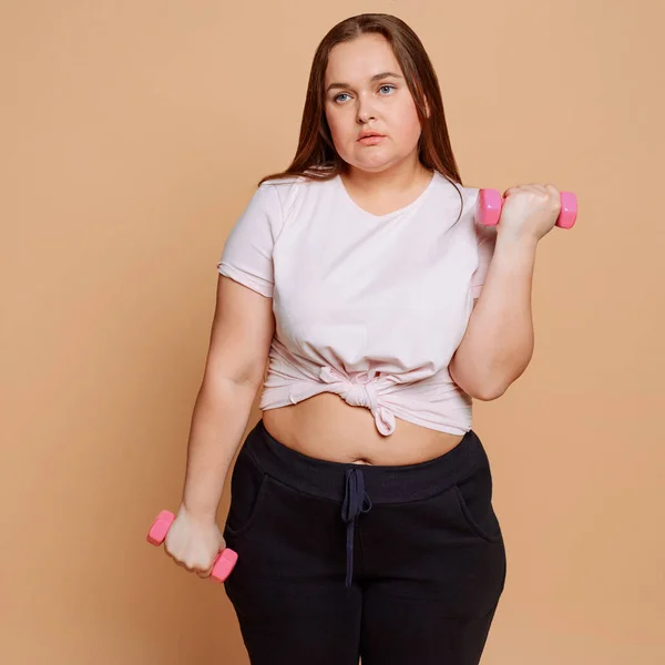 Скучная женщина с избыточным весом работает с гантелями неохотно — стоковое фото