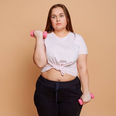 Bej arka planda istemeden dambıl egzersizi yapan sıkıcı kız.