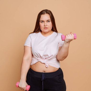 Şişman kadın bej arka planda dambıl egzersizi yapıyor.