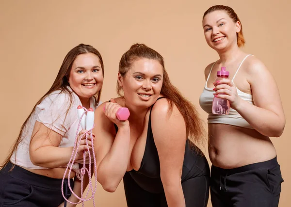 Overweight girls at the gym. Portrait on beige background