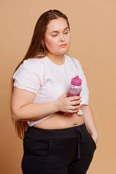 Mulher com excesso de peso com uma garrafa de água no fundo bege — Fotografia de Stock