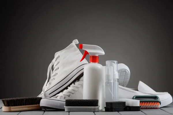 Calçado branco e suprimentos de limpeza em fundo cinza — Fotografia de Stock