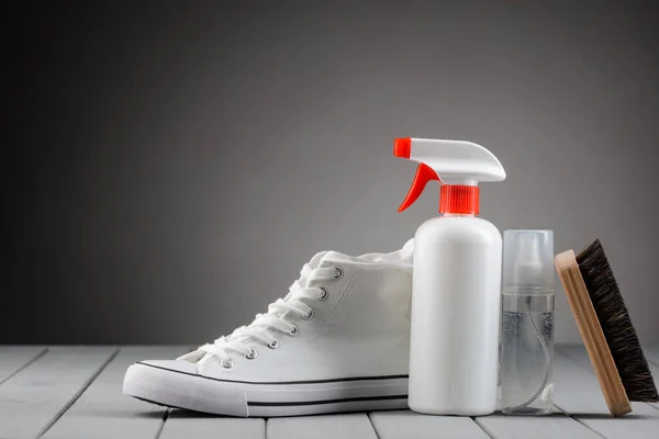 Zapatilla blanca, spray limpiador y cepillo sobre fondo gris — Foto de Stock