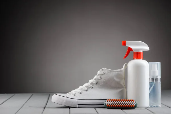 Zapatilla de lona blanca y suministros para el cuidado del calzado sobre fondo gris — Foto de Stock