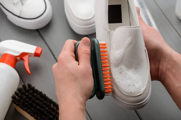 Hombre limpiando mocasines blancos con un cepillo y detergente — Foto de Stock