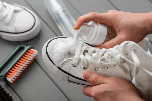 Man spraying cleaner foam onto a white sneaker, closeup shot