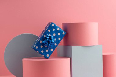Mavi benekli hediye kutusu silindirler üzerinde ve küp pembe arka planda