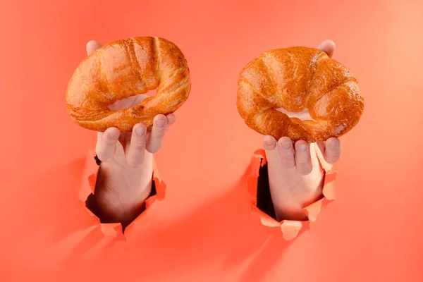 Mãos segurando dois croissants através de buracos rasgados no fundo de papel vermelho — Fotografia de Stock