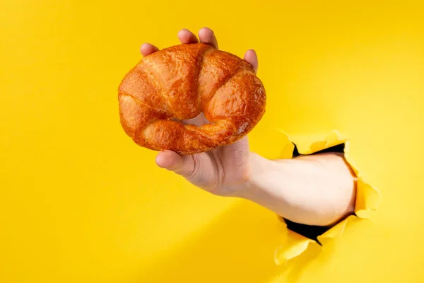 Hand showing a freshly baked croissant on yellow background — Stock Photo, Image