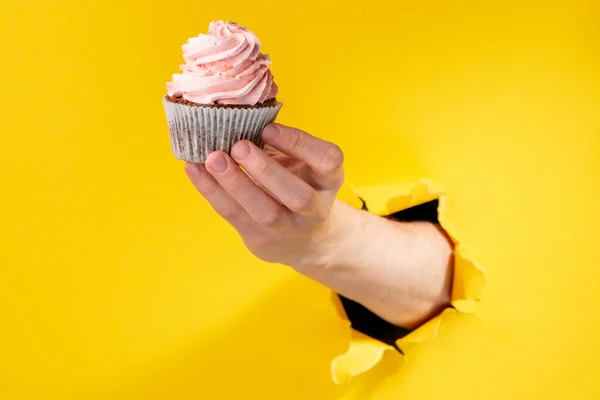 Hand hålla en cupcake med rosa smörkräm virvel — Stockfoto