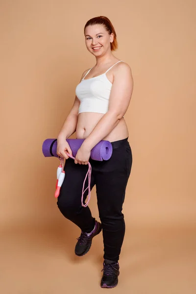 Jovem mulher com sobrepeso com equipamento de fitness em fundo bege — Fotografia de Stock