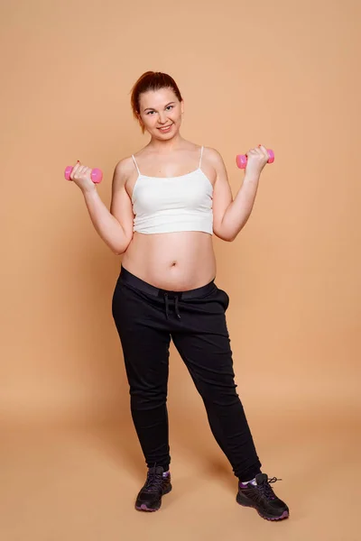 Mulher com excesso de peso fazendo exercícios de halteres no fundo bege — Fotografia de Stock