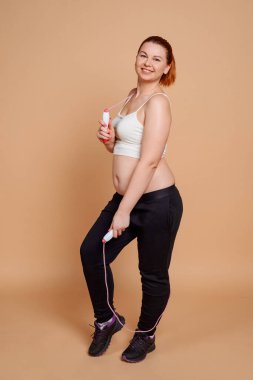 Bej arka planda atlama ipiyle poz veren şişman kadın.