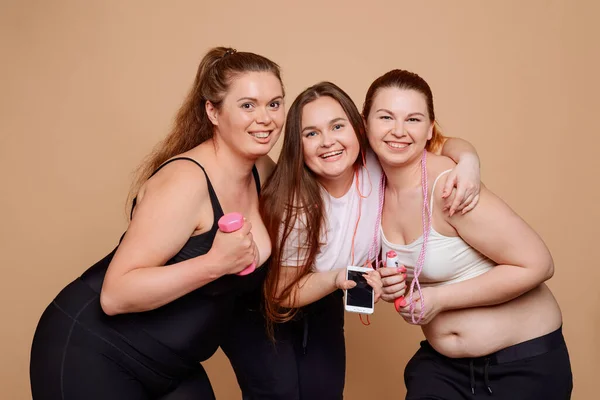 Plus size girls posing on beige background after fitness classes