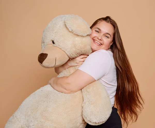 Grown woman hugging a huge Teddy bear on beige background