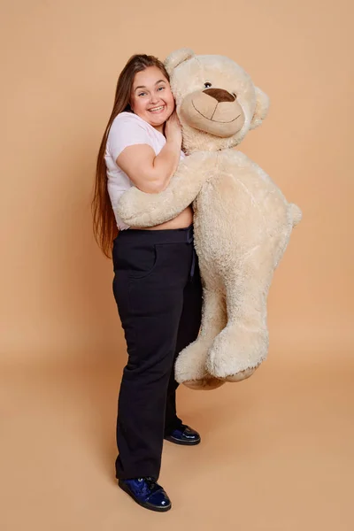 Happy woman hugging Teddy bear on beige background