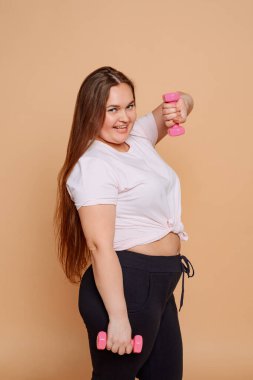 Artı bej arka planda pembe halterli poz veren boyda bir kız.