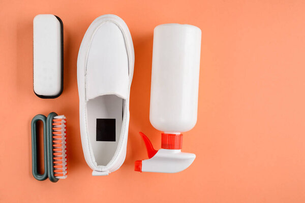 White shoe, brushes and cleanser spray on orange background