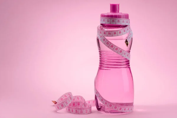 Meça fita e garrafa de água no fundo rosa — Fotografia de Stock