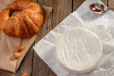Kruvasan, Camembert peyniri, ahşap masada reçel ve badem.