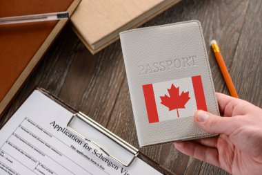 Elinde Kanada pasaportu, arka planda bir başvuru formu var.