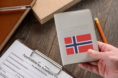 Elinde Norveç pasaportu, arka planda bir başvuru formu var.