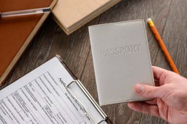 Elinde pasaport, arka planda başvuru formu var.