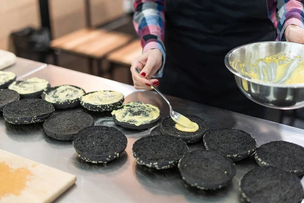 Vrouw zet kaassaus op zwarte broodjes — Stockfoto