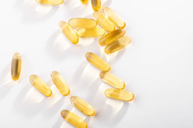 Sarı kapsüller beyaz arkaplan üzerine dağılmış, üst görünüm.