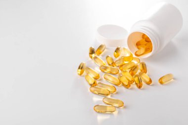 Sarı kapsüller beyaz arka planda bir şişeden yayılmış.