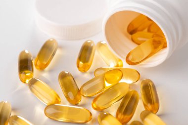 Beyaz arka plandaki bir şişeden yayılmış sarı kapsüllere yakın çekim