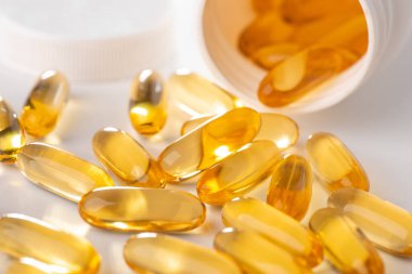 Beyaz arka plandaki bir şişeden yayılmış morina yağı kapsüllerine yakın plan.