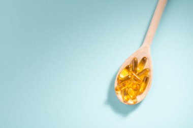 Mavi arka planda tahta kaşık Omega-3 kapsülleri