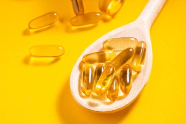 Turuncu arka planda ahşap bir kaşık morina yağı kapsülüne yakın plan.