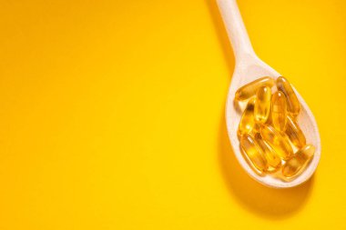 Turuncu arka planda, tahta kaşık Omega-3 kapsülleri ve kopyalama alanı